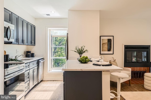 108 W Barre St Unit R 48, Baltimore, MD 21201 - kitchen featuring appliances with stainless steel finishes, light wood finished floors, a breakfast bar, a kitchen island, and light stone countertops