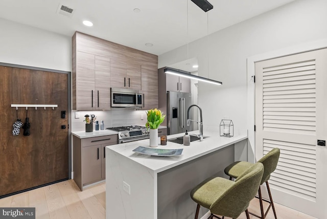 1471 Harvard St NW Unit 2, Washington, DC 20009 - kitchen featuring appliances with stainless steel finishes, a breakfast bar area, decorative backsplash, a peninsula, and light countertops