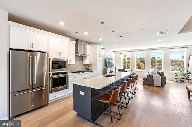 324 Star Tavern Ln, West Chester, PA 19382 - kitchen featuring appliances with stainless steel finishes, wall chimney exhaust hood, white cabinetry, a kitchen island with sink, and a kitchen breakfast bar
