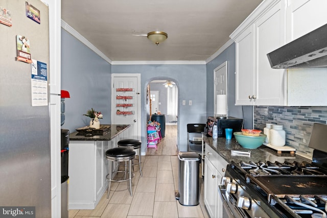 330 N 13th St, Reading, PA 19604 - kitchen featuring stainless steel appliances, wall chimney exhaust hood, arched walkways, white cabinetry, and crown molding
