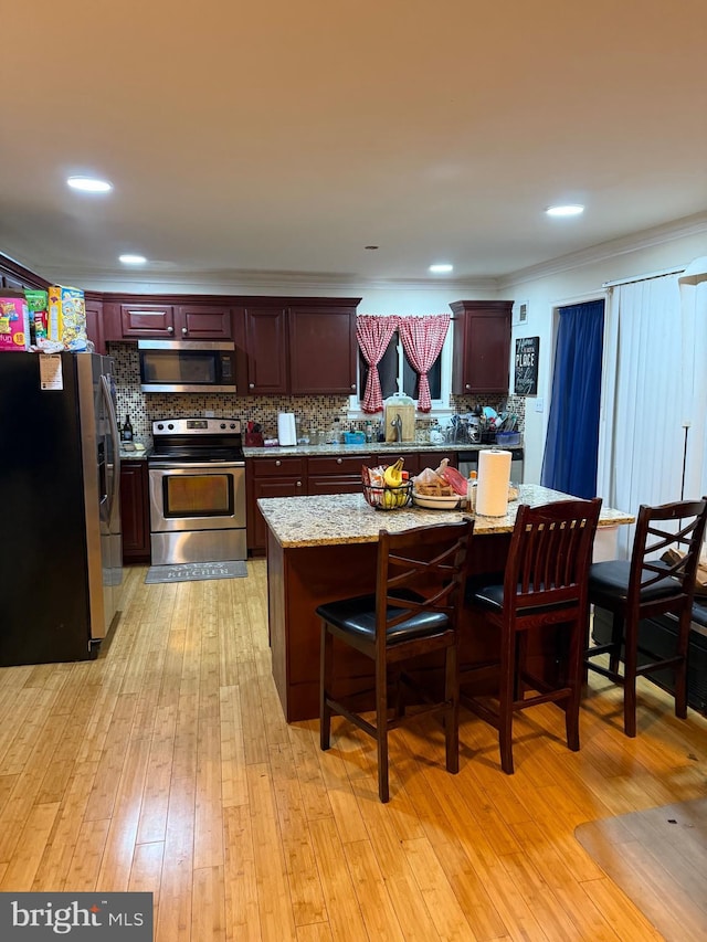 16820 Malabar St, Rockville, MD 20855 - kitchen featuring appliances with stainless steel finishes, decorative backsplash, a kitchen bar, light wood-style floors, and light stone counters