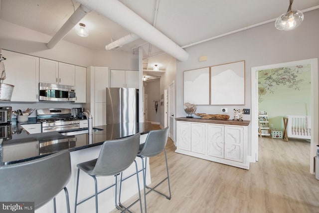 4480 Market Commons Dr Unit 215, Fairfax, VA 22033 - kitchen with appliances with stainless steel finishes, dark countertops, white cabinets, light wood-style flooring, and a kitchen bar