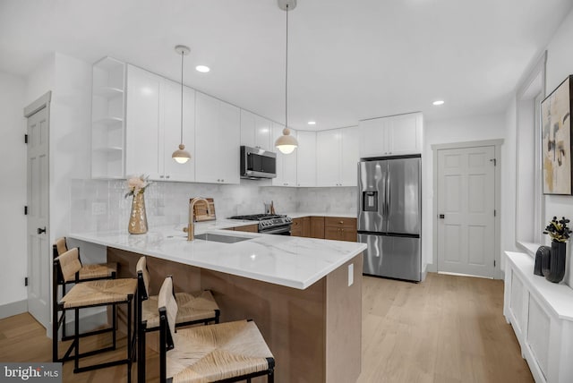 136 W 3rd Ave, Conshohocken, PA 19428 - kitchen with stainless steel appliances, open shelves, a peninsula, light wood-type flooring, and a breakfast bar area