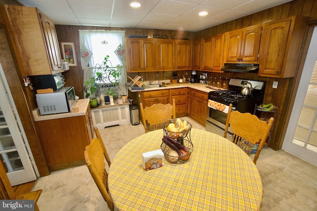 4425 E Howell St, Philadelphia, PA 19135 - kitchen with gas stove, under cabinet range hood, brown cabinetry, radiator, and light countertops