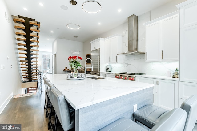 1217 Bainbridge St, Philadelphia, PA 19147 - kitchen featuring wall chimney exhaust hood, a center island with sink, backsplash, wood finished floors, and white cabinets