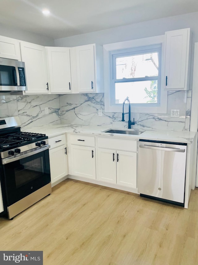 213 N Willow St, Gloucester City, NJ 08030 - kitchen featuring appliances with stainless steel finishes, light stone countertops, white cabinetry, light wood-style floors, and decorative backsplash