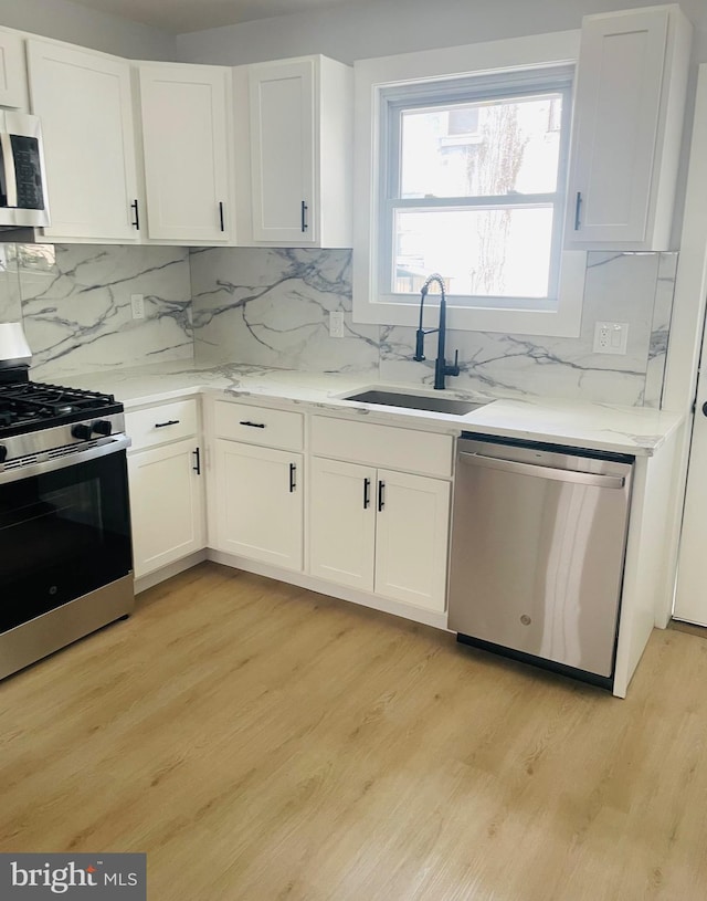 213 N Willow St, Gloucester City, NJ 08030 - kitchen featuring appliances with stainless steel finishes, white cabinetry, tasteful backsplash, and light wood-type flooring