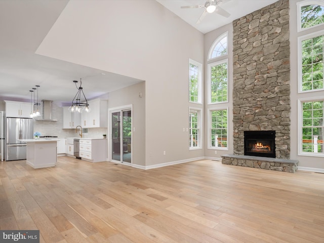 1015 S Creek View Ct, Churchton, MD 20733 - unfurnished living room featuring light wood-style flooring, ceiling fan, a towering ceiling, and a fireplace