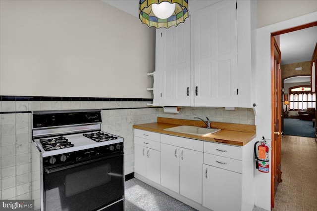 1243 Buttonwood St, Reading, PA 19604 - kitchen featuring black gas range oven, white cabinetry, tile walls, light countertops, and arched walkways