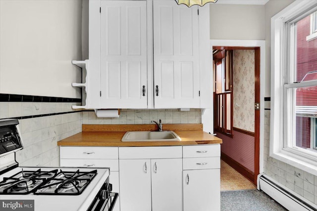 1243 Buttonwood St, Reading, PA 19604 - kitchen featuring baseboard heating, white gas stove, white cabinetry, wainscoting, and wallpapered walls