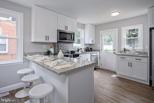 8207 Rockdale Ave, Baltimore, MD 21244 - kitchen with appliances with stainless steel finishes, white cabinets, wood finished floors, light stone countertops, and a kitchen bar