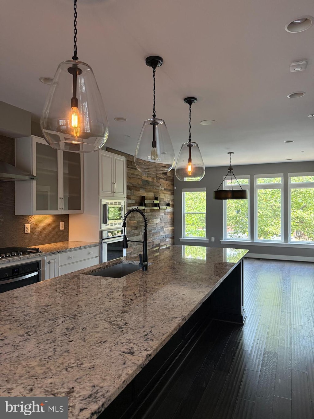 42391 Willow Creek Way, Brambleton, VA 20148 - kitchen featuring appliances with stainless steel finishes, backsplash, light stone countertops, glass insert cabinets, and white cabinetry