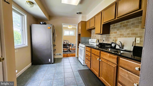 4753 Pomponio Pl, Annandale, VA 22003 - kitchen featuring freestanding refrigerator, white range with gas stovetop, backsplash, light tile patterned floors, and brown cabinetry