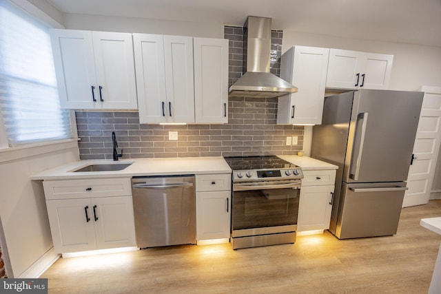 7127 Woolston Ave, Philadelphia, PA 19138 - kitchen featuring appliances with stainless steel finishes, wall chimney range hood, light wood finished floors, and white cabinetry