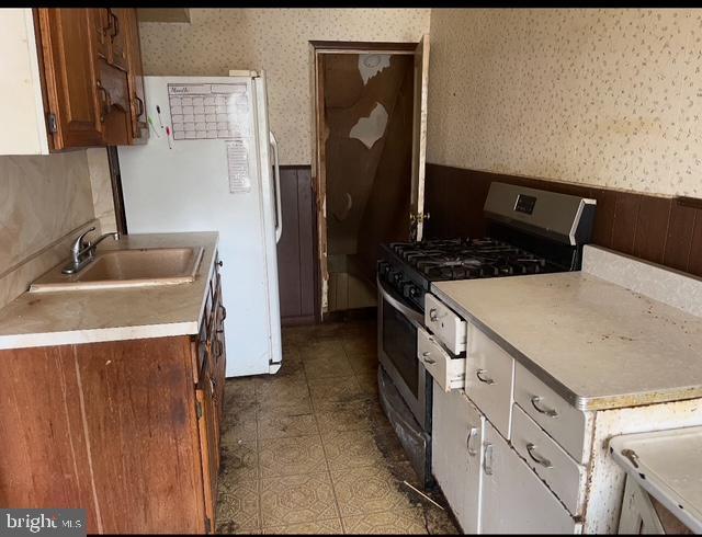 6530 Algard St, Philadelphia, PA 19135 - kitchen featuring wallpapered walls, stainless steel gas range, wainscoting, light countertops, and freestanding refrigerator