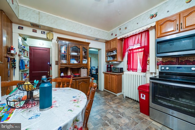 930 Elm St, Reading, PA 19601 - kitchen with radiator, appliances with stainless steel finishes, ornamental molding, brown cabinetry, and stone finish flooring