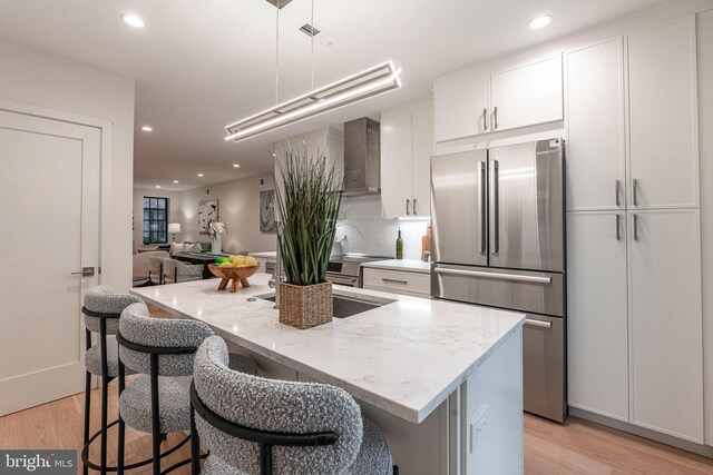 2005 Saint Albans St, Philadelphia, PA 19146 - kitchen with freestanding refrigerator, wall chimney exhaust hood, light wood-type flooring, white cabinetry, and a breakfast bar area