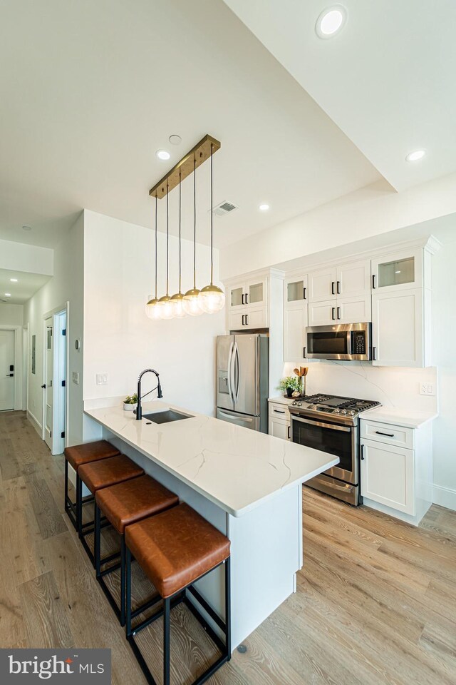 2517 Ontario Rd NW Unit Ph7, Washington, DC 20009 - kitchen with appliances with stainless steel finishes, white cabinets, a breakfast bar, light wood finished floors, and light stone counters