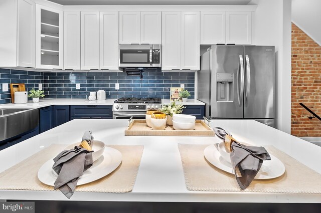 3306 E Lombard St, Baltimore, MD 21224 - kitchen featuring stainless steel appliances, white cabinets, blue cabinets, glass insert cabinets, and brick wall