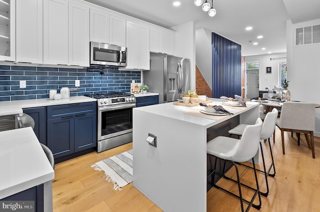 3306 E Lombard St, Baltimore, MD 21224 - kitchen with stainless steel appliances, blue cabinets, light wood-style flooring, white cabinets, and a kitchen breakfast bar