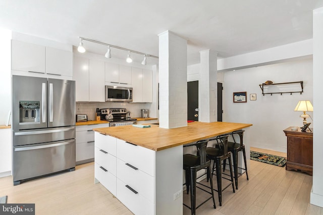4301 Massachusetts Ave NW Unit A212, Washington, DC 20016 - kitchen with appliances with stainless steel finishes, wooden counters, a kitchen bar, light wood-style flooring, and white cabinets