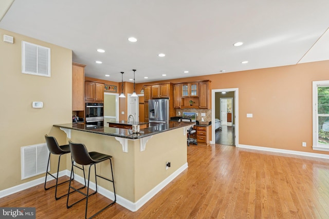 1340 Mountain View Rd, Stafford, VA 22554 - kitchen with stainless steel appliances, brown cabinetry, a breakfast bar area, a peninsula, and light wood-type flooring