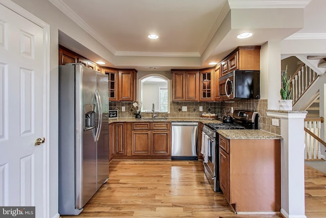 9009 Marie Ct, Lorton, VA 22079 - kitchen featuring appliances with stainless steel finishes, brown cabinetry, light wood-style floors, glass insert cabinets, and light stone countertops
