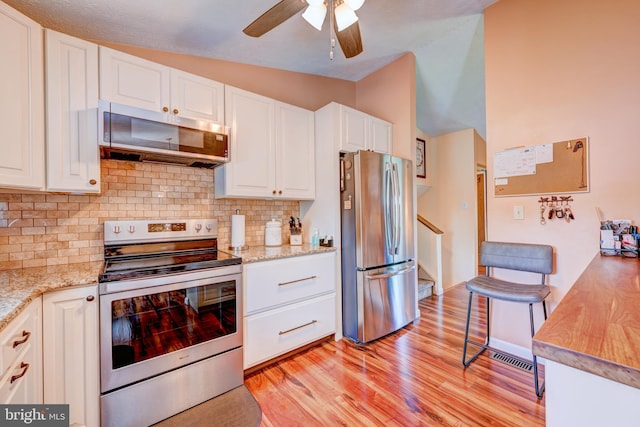 169 Independence Dr, Morrisville, PA 19067 - kitchen with stainless steel appliances, vaulted ceiling, white cabinets, light wood-type flooring, and tasteful backsplash
