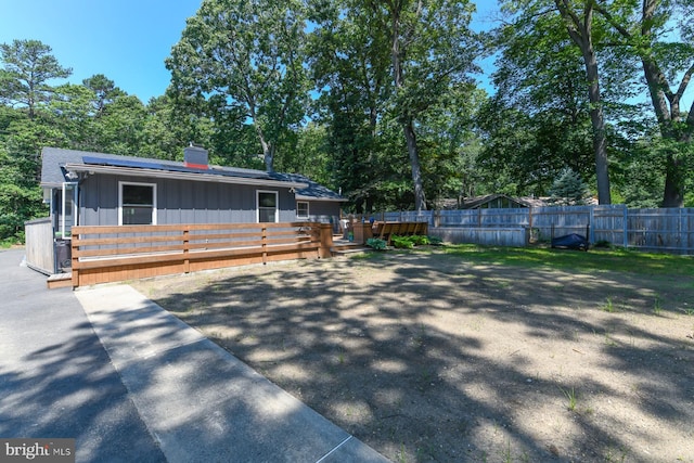 513 N E Ave, Wenonah, NJ 08090 - view of front of property with board and batten siding, a deck, a chimney, roof mounted solar panels, and view of wooded area