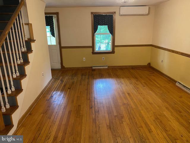 21 Willow St, Milroy, PA 17063 - empty room featuring a wall unit AC, hardwood / wood-style flooring, plenty of natural light, and stairway