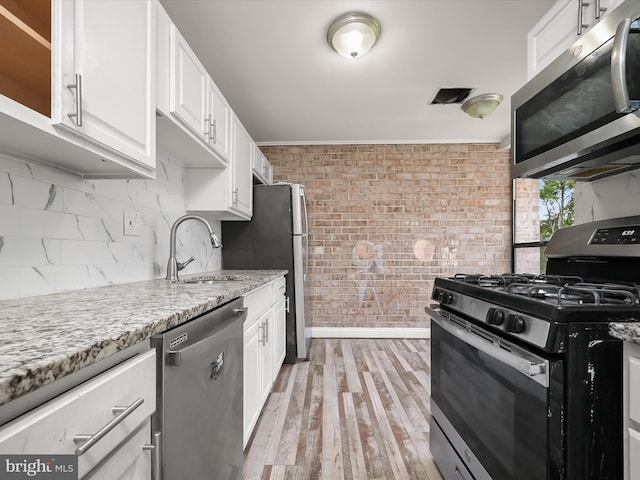 3316 Huntley Square Dr Unit A1, Temple Hills, MD 20748 - kitchen with stainless steel appliances, white cabinets, brick wall, light wood finished floors, and light stone countertops