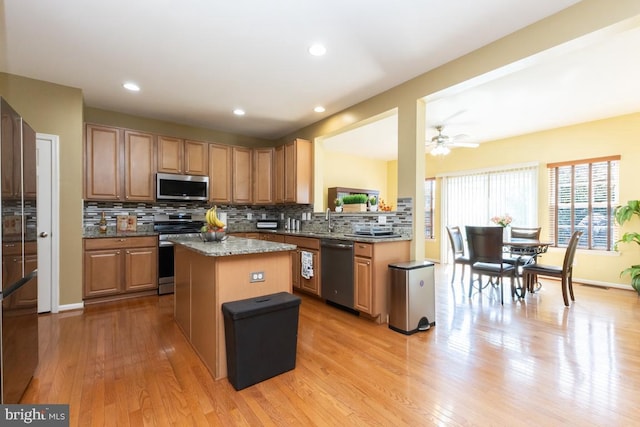 16435 Regatta Ln, Woodbridge, VA 22191 - kitchen with appliances with stainless steel finishes, a center island, decorative backsplash, light wood finished floors, and light stone counters