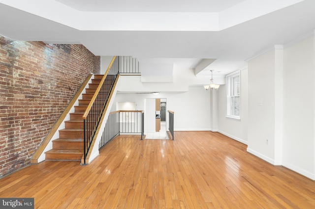 1401 Druid Hill Ave, Baltimore, MD 21217 - unfurnished living room featuring brick wall, light wood-type flooring, a chandelier, and stairway