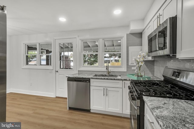 1700 Melbourne Rd, Baltimore, MD 21222 - kitchen featuring appliances with stainless steel finishes, light stone counters, decorative backsplash, white cabinets, and light wood finished floors