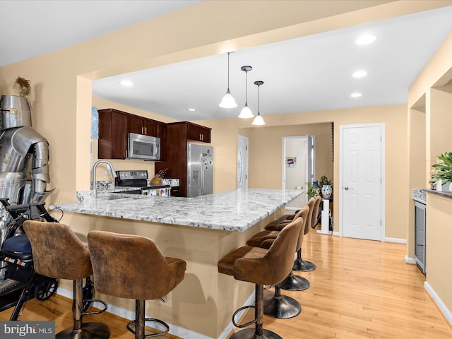 1811 Hilltop Ave, Baltimore, MD 21221 - kitchen with appliances with stainless steel finishes, a peninsula, light wood finished floors, a breakfast bar, and light stone counters