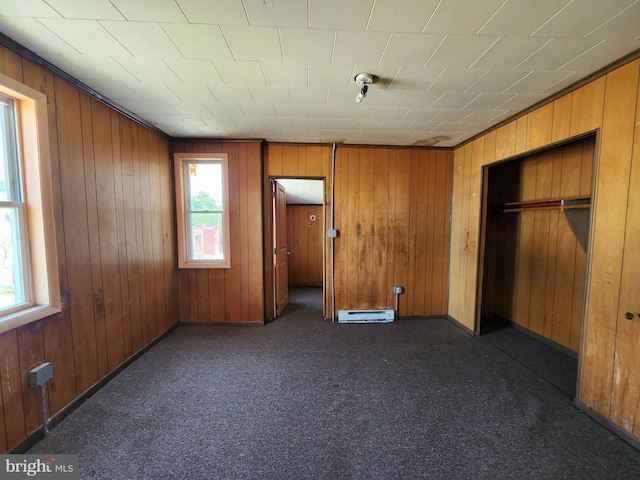 101 S Payson St, Baltimore, MD 21223 - unfurnished bedroom featuring wooden walls, a baseboard heating unit, dark colored carpet, and a closet