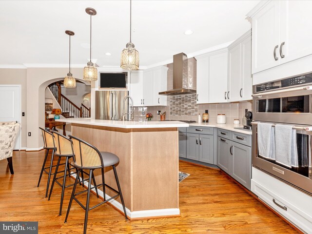 2503 Island Grove Blvd, Frederick, MD 21701 - kitchen featuring gray cabinetry, wall chimney range hood, stainless steel appliances, light countertops, and a kitchen bar