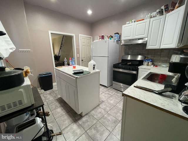 3102 N Taylor St, Philadelphia, PA 19132 - kitchen with gas range, freestanding refrigerator, under cabinet range hood, tasteful backsplash, and white cabinetry