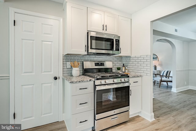147 Meadowbrook Ave, Upper Darby, PA 19082 - kitchen featuring stainless steel appliances, arched walkways, light stone countertops, backsplash, and white cabinets