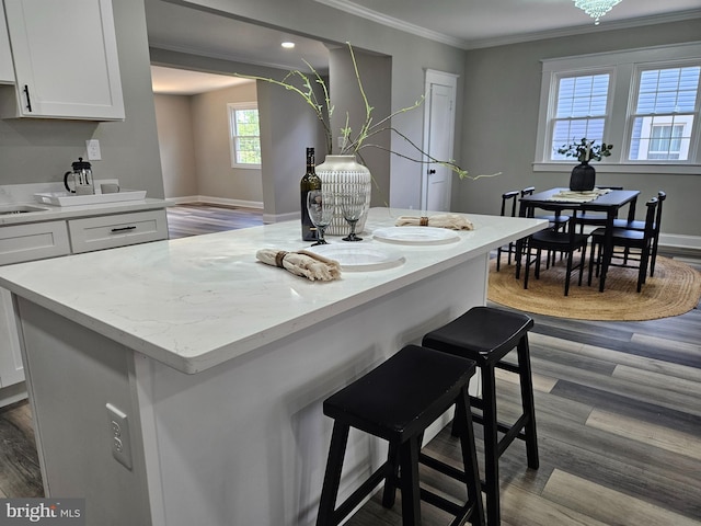 2900 Westfield Ave, Baltimore, MD 21214 - kitchen featuring ornamental molding, white cabinetry, wood finished floors, a breakfast bar area, and light stone countertops
