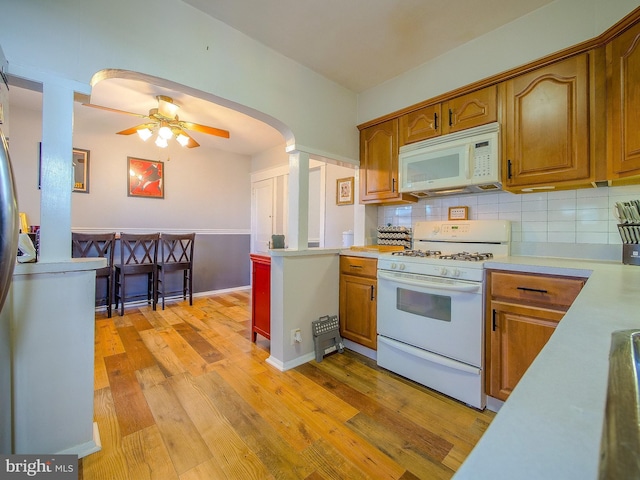 121 Wayne Ave, Springfield, PA 19064 - kitchen featuring white appliances, light countertops, light wood finished floors, decorative backsplash, and brown cabinetry