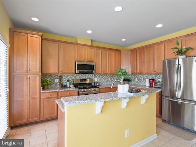 43559 Wheadon Ter, Chantilly, VA 20152 - kitchen featuring stainless steel appliances, light tile patterned flooring, a center island with sink, a kitchen breakfast bar, and light stone counters