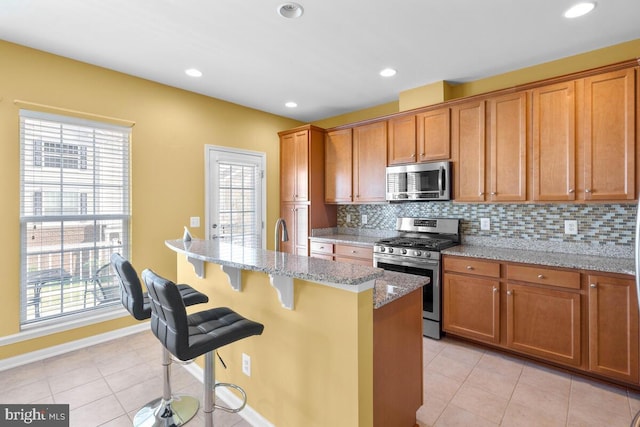 43559 Wheadon Ter, Chantilly, VA 20152 - kitchen featuring appliances with stainless steel finishes, a kitchen bar, light stone counters, tasteful backsplash, and plenty of natural light