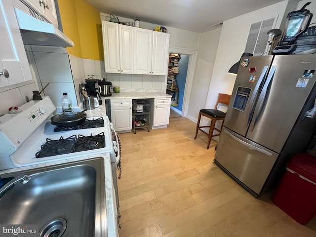 713 E 23rd St, Baltimore, MD 21218 - kitchen with stainless steel refrigerator with ice dispenser, under cabinet range hood, white range with gas cooktop, light countertops, and light wood finished floors