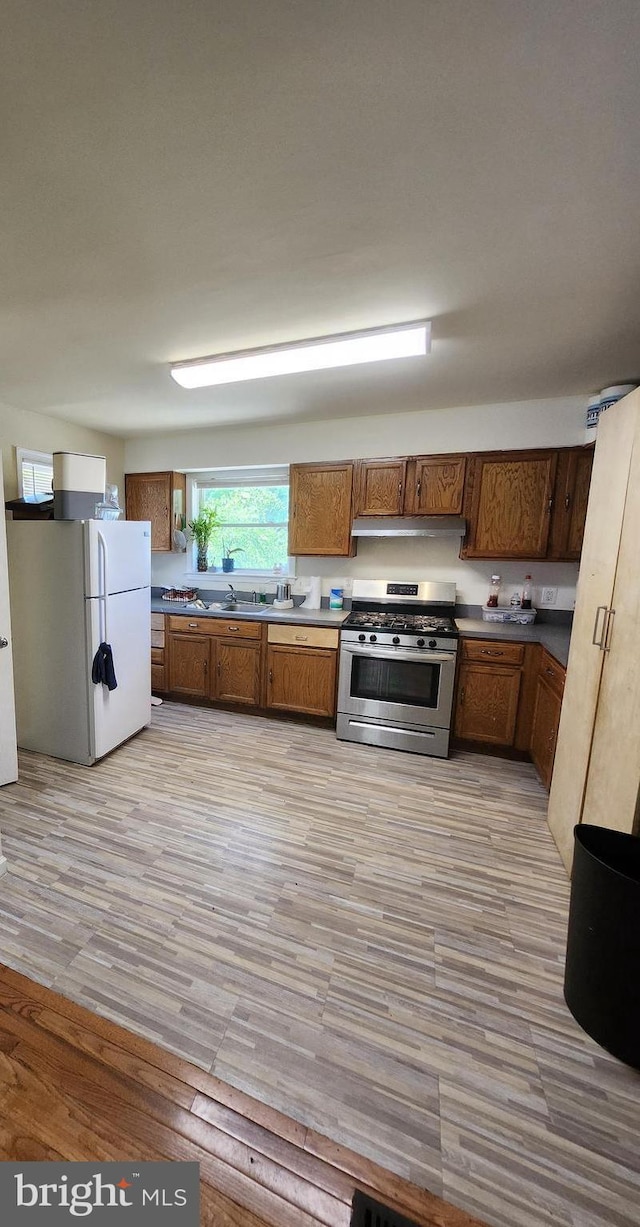 5503 Lanham Station Rd, Lanham, MD 20706 - kitchen with gas range, freestanding refrigerator, under cabinet range hood, light wood-style flooring, and brown cabinetry
