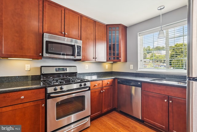 4163 S Four Mile Run Dr Unit 401, Arlington, VA 22204 - kitchen featuring appliances with stainless steel finishes, light wood finished floors, glass insert cabinets, hanging light fixtures, and dark stone counters