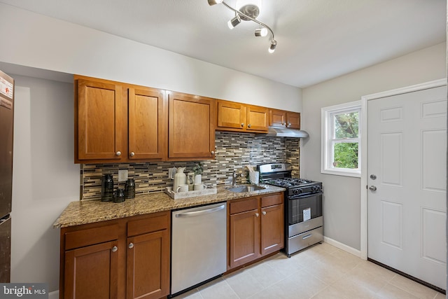 4703 Williston St, Baltimore, MD 21229 - kitchen featuring stainless steel appliances, decorative backsplash, brown cabinetry, and under cabinet range hood