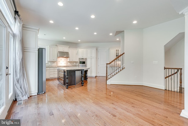 10002 Courthouse Rd, Vienna, VA 22181 - kitchen featuring appliances with stainless steel finishes, under cabinet range hood, a kitchen breakfast bar, tasteful backsplash, and a center island