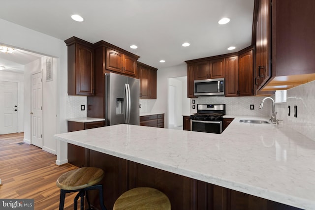 27 Brown Cir, Fredericksburg, VA 22405 - kitchen featuring stainless steel appliances, a peninsula, decorative backsplash, light stone counters, and light wood-style flooring