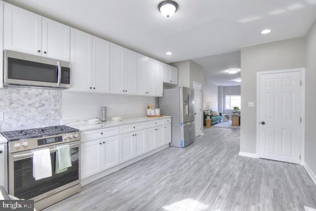 429 N Lakewood Ave, Baltimore, MD 21224 - kitchen featuring stainless steel appliances, light wood-type flooring, white cabinetry, tasteful backsplash, and light stone countertops